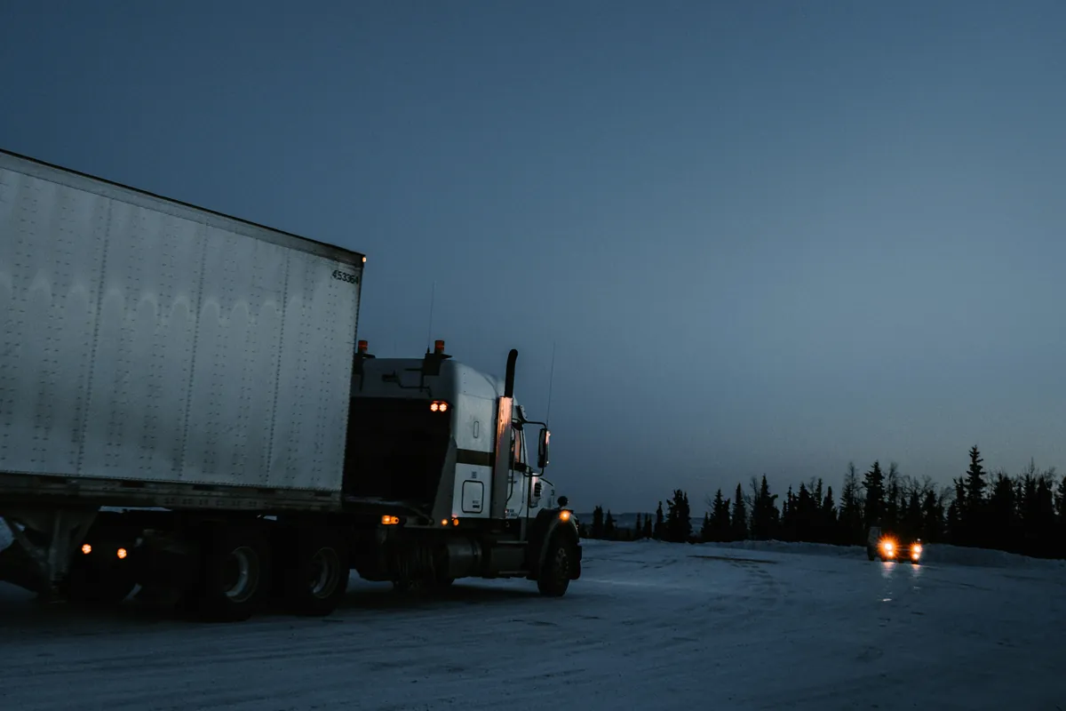 A truck and trailer on a snowy road at dusk